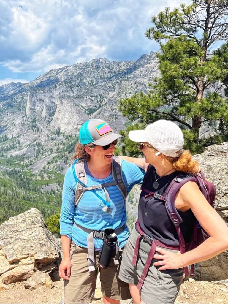 Two woman friends laughing at the Blodgett Canyon Overlook in Montana in the Bitterroot National Forest. Credit: Gatherandgotravel.com