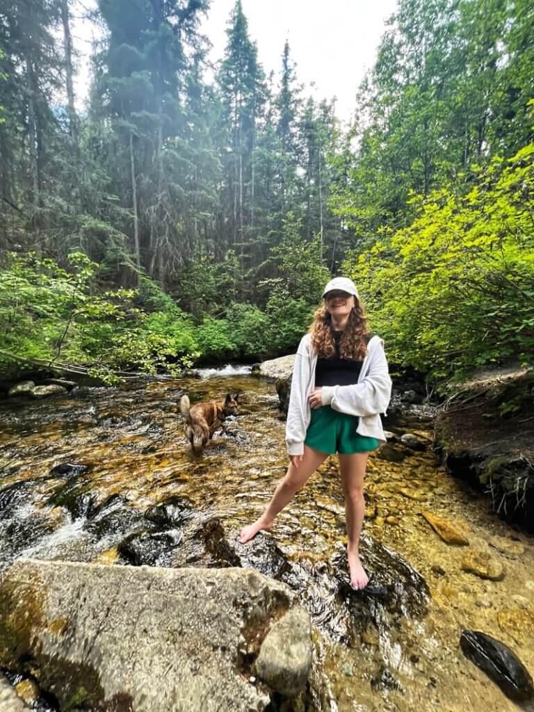 Young woman standing in a creek with a dog near the Blodgett Canyon trailhead in Montana. Credit: Gatherandgotravel.com